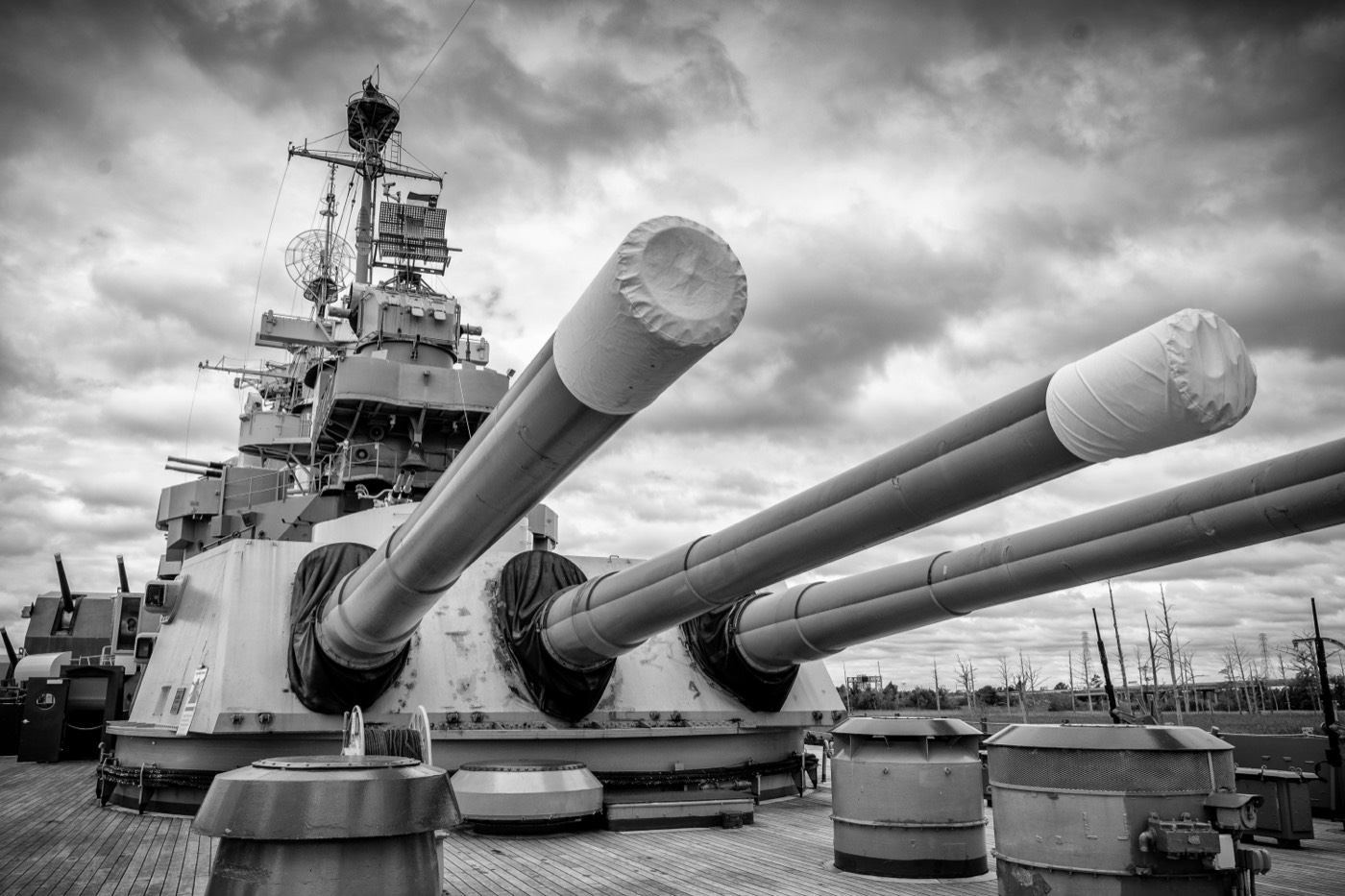 Gun turrets on the deck of a battleship under a cloudy sky.